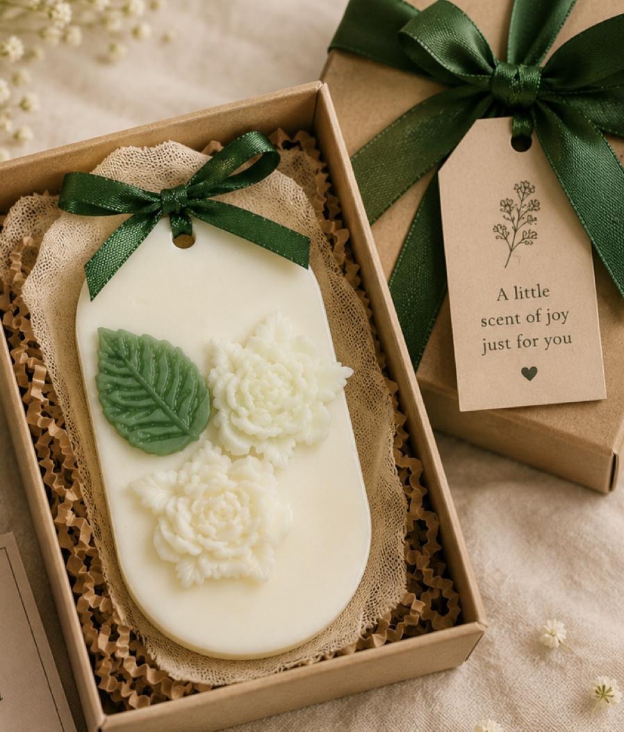 White botanical wax plaque with green leaves and flowers inside a ribboned gift box