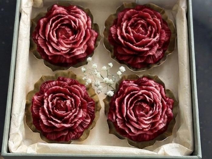 Four deep red rose-shaped candles in a presentation box